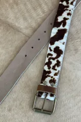 Cinturón de cuero con estampado animal print blanco y negro, hebilla metálica plateada y pasador de cuero negro.