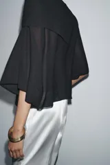 Top color crema de tejido de punto, con cuello asimétrico y mangas anchas.