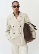 Anorak color beige con cuello de pico con solapa, manga larga con trabillas, cierre de doble botonadura y dos bolsillos laterales.