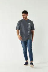 Remera gris oscuro de manga corta con estampado rectangular en el frente que incluye texto y figuras geométricas en blanco y verde.
