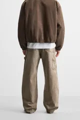 Pantalón color marrón con efecto lavado, corte relaxed fit, cinco bolsillos, aplicación de tira y bolsillo multifunción en perneras, cierre frontal con cremallera y botón.