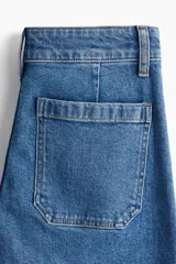 Pantalón de jean de algodón con leve stretch, tiro alto y pierna ancha. Presenta bolsillos de parche cuadrados en la parte delantera y bolsillos traseros. El lavado es celeste medio con efecto de desgaste vertical en las piernas.
