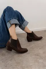 Botín negro de cuero con paneles laterales de gamuza y elástico en los tobillos. Tiene un pequeño taco cuadrado.