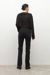 Jean negro de tiro medio, corte bootcut, con tachas metálicas plateadas decorando los laterales de las piernas y el ruedo.