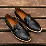 Mocasín negro de cuero vacuno, con interior de cuero, taco de madera foliado en cuero de 2,5 cm, entre suela de goma de 1 cm y horma de punta redonda.