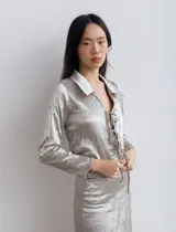Camisa de seda color plateado, con cuello clásico, mangas largas y lazos para anudar en el frente.