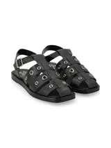 Sandalia tipo cangrejera en cuero graneado color negro, con ornamentos metálicos y hebilla ajustable.
