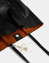 Cartera shopper negra de cuerina con manijas superiores y acceso mediante broche imantado. Incluye charm de perlas en forma de moño.
