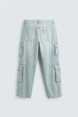 Pantalón de denim color beige, corte relaxed fit, con bolsillos laterales tipo cargo con solapa y cierre de botón. Cierre frontal con botón y cremallera.