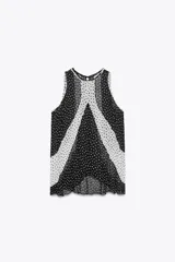 Top de cuello redondo y manga sisa con detalle de tejido plisado semitransparente y estampado de lunares blancos y negros. Bajo asimétrico y cierre en espalda con abertura y botón.
