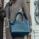 Cartera tipo tote color azul con diseño calado. Tiene doble asa corta trenzada y correa larga regulable extraíble. Cuenta con un compartimento principal con cierre, un bolsillo interno con cierre y dos bolsillos abiertos.