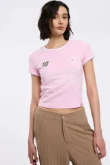 Remera corta rosa con cuello y mangas con ribete blanco, estampado frontal con la frase 'Game Over' y detalles de números y estrellas.