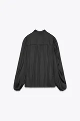 Camisa fluida negra de cuello redondo con lazada, manga larga tipo globo con pliegues en hombro y cierre frontal con botones ocultos por solapa.