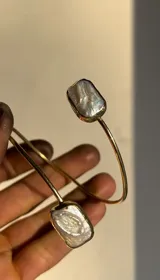 Pulsera rígida abierta de bronce dorado con dos perlas barrocas rectangulares en los extremos.