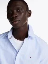 Camisa celeste con rayas verticales, de corte regular, cuello abotonado, mangas largas con puños abotonados y logo de la marca bordado en el pecho.
