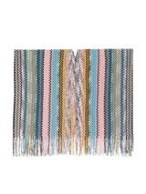 Capa tipo poncho de tejido de punto con diseño de zigzag multicolor en tonos amarillo, gris, negro y beige. Presenta cuello en V y flecos en el borde inferior.