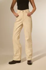 Pantalón de jean color beige claro, tiro alto y corte recto. Presenta detalles de strass o apliques brillantes distribuidos por toda la prenda.