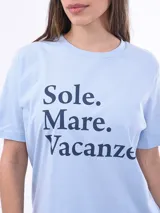 Remera negra de algodón con cuello redondo y mangas cortas. Estampado frontal con la frase "World Tour Vacation State of Mind" en letras de colores y un pequeño dibujo de una palmera.