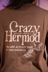 Remera oversize marrón de algodón elastizado con estampado en la espalda que incluye el texto "Crazy Hermod movement" y un diseño de zapatilla alada.