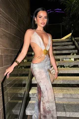 Vestido largo con estampado abstracto en tonos grises, celestes y marrones. Presenta escote halter con abertura en el abdomen unida por un adorno de concha.