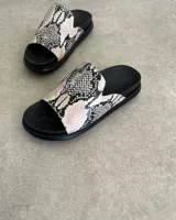 Sandalias chatas color beige con base negra y detalle de bordado blanco en la tira superior.