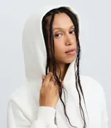 Buzo femenino color blanco crema, confeccionado en algodón y poliéster, con capucha estructurada, bolsillo canguro delantero y puños acanalados.