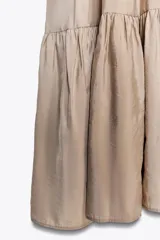 Vestido midi color beige de tejido fluido con escote pico, tirantes finos ajustables y bajo acabado en paneles con pliegues.