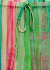 Pantalón de tejido fluido con estampado de rayas verticales en tonos verde, rojo, amarillo y celeste. Diseño recto, largo y semitransparente, con cintura elástica y lazo de ajuste.