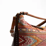 Bolso tipo hobo con estampado geométrico multicolor y detalles de tachas en los bordes.