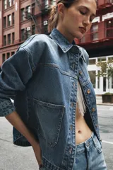Cazadora de denim celeste de corte recto, con cuello solapa, manga larga, bolsillos delanteros de plastrón y cierre frontal con botones metálicos.