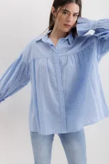 Camisa gris a rayas verticales blancas, de corte amplio, cuello alto con lazo y mangas largas abullonadas con puños elásticos.
