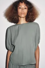 Blusa de cuello redondo color verde, confeccionada en hilatura con mezcla de lyocell. Manga corta abullonada ajustable con lazadas. Bajo redondeado.