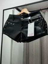 Mini short negro de cuero sintético con tachas plateadas en forma de oso en los bolsillos delanteros y ojales metálicos en los laterales.