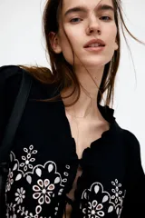 Blusa cropped de algodón color negro con bordado de flores blancas, mangas largas abullonadas, escote en V con volados y cierre frontal con lazos.