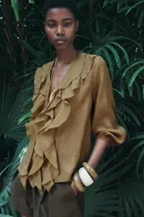 Camisa color verde oliva de tela traslúcida con escote en V, mangas largas abullonadas con puños elásticos y volantes en el frente.