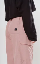 Pantalón cargo rosa con cintura elastizada y cordón ajustable. Botamangas ajustables con cordón elástico y tancas.