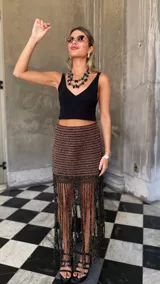 Falda corta tejida a mano en crochet, con diseño a rayas horizontales en tonos marrón oscuro y dorado brillante. Presenta un borde inferior con flecos largos y abundantes.