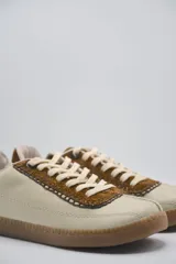 Zapatillas bajas color beige con detalles en marrón y cordones blancos.