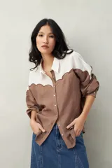 Camisa de lino color marrón y blanco, con corte recto, cuello camisero, mangas largas con puños abotonados y cierre frontal con botones. Presenta canesú con diseño ondulado.