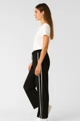 Pantalón negro ancho con rayas blancas laterales y cintura elastizada con cordón ajustable.