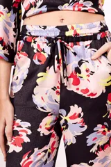 Conjunto de pantalón y top de viscosa con estampado floral en tonos rosa, celeste, amarillo y rojo sobre fondo negro. El top es cruzado con mangas acampanadas y el pantalón es de corte palazzo con cintura elastizada.