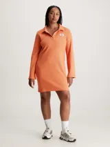 Vestido corto naranja de punto de algodón elástico con textura de canalé. Tiene cuello polo en V, mangas largas acampanadas e insignia con el monograma de Calvin Klein en el pecho.