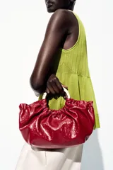 Bolso de mano fruncido color rojo con doble asa metálica dorada. Incluye bolsillo interior con cierre y asa bandolera extraíble.
