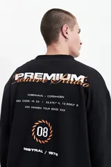 Buzo de felpa negro con estampado en la espalda que incluye la palabra 'Premium' en blanco y naranja, la frase 'Creative Studio' en naranja, y otros textos y gráficos en blanco y naranja. Tiene cuello redondo y puños.