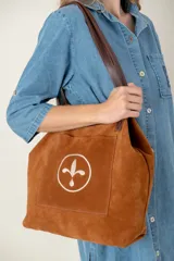 Bolso tipo tote bag de gamuza azul con asas de cuero marrón y bolsillo externo con logo bordado.