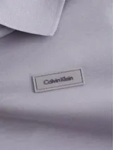 Chomba color lila de algodón orgánico, corte slim, cuello clásico con dos botones, mangas cortas con puños de punto, aberturas laterales y logo de Calvin Klein bordado en el pecho.