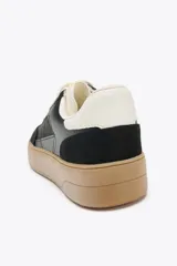 Zapatillas deportivas de mujer con combinación de materiales en negro, blanco y marrón. Cierre con cordones y suela en contraste color caramelo.