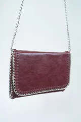 Bandolera color borgoña con textura símil cuero, cadena plateada y pespuntes decorativos.
