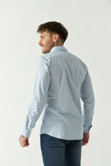 Camisa de hombre a rayas verticales celestes y blancas, corte slim fit, manga larga, logo bordado en el pecho y cartera con botones.