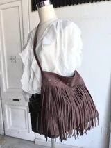 Bandolera marrón con flecos largos y detalles de ojales metálicos.